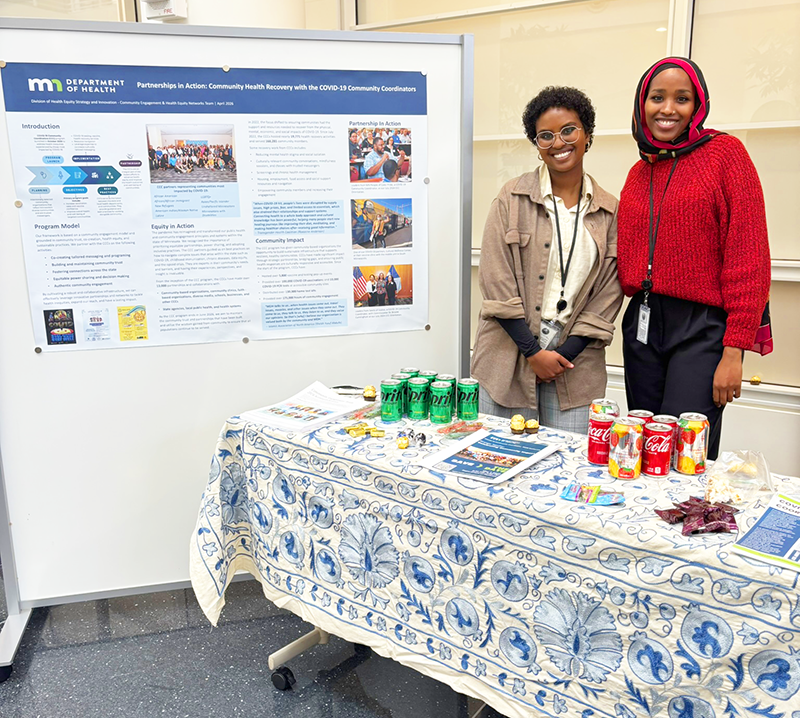 Two HESI staff smile for a photo next to the CCC poster at the showcase