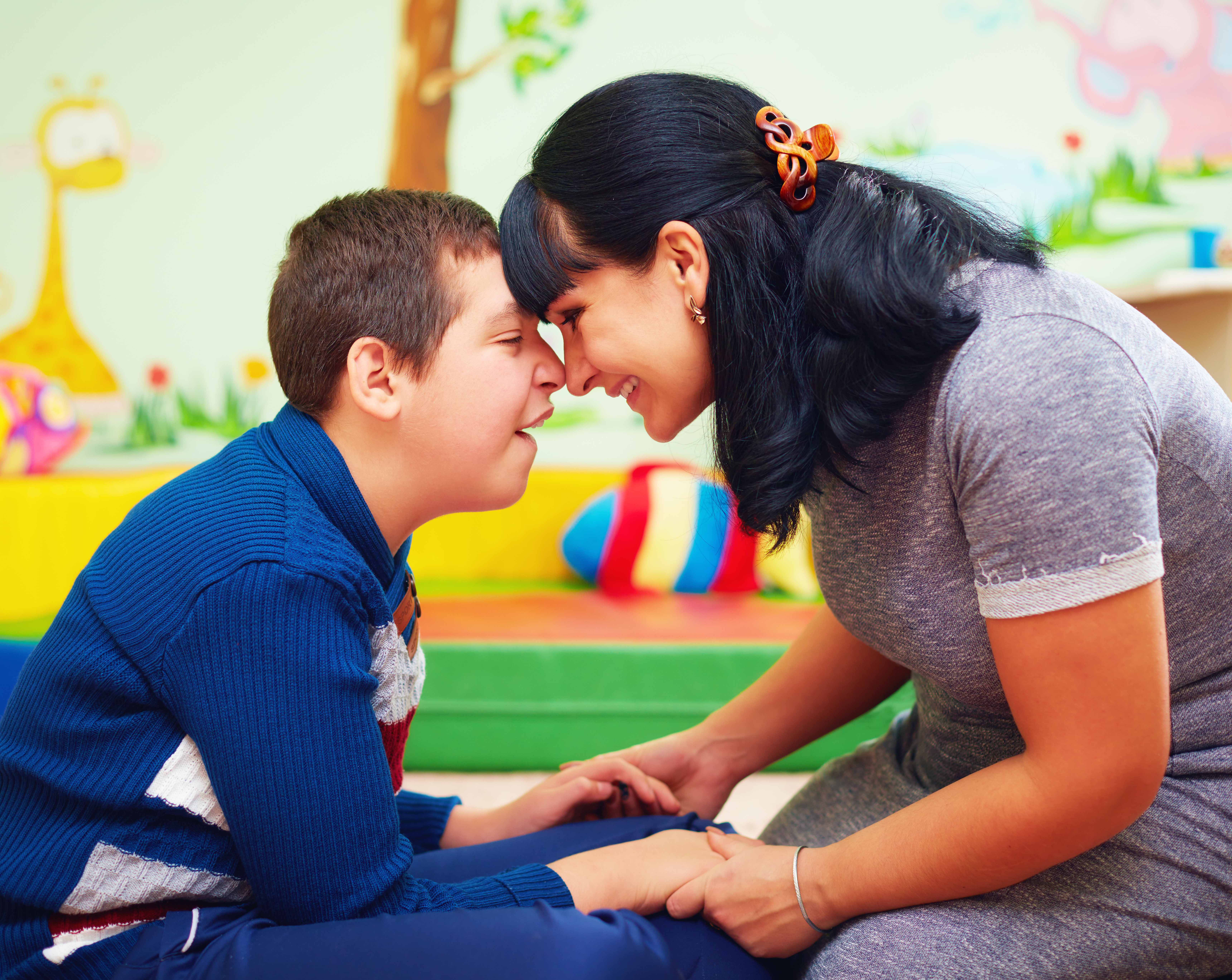caregiver sits on the ground and connects with a young boy with a disability