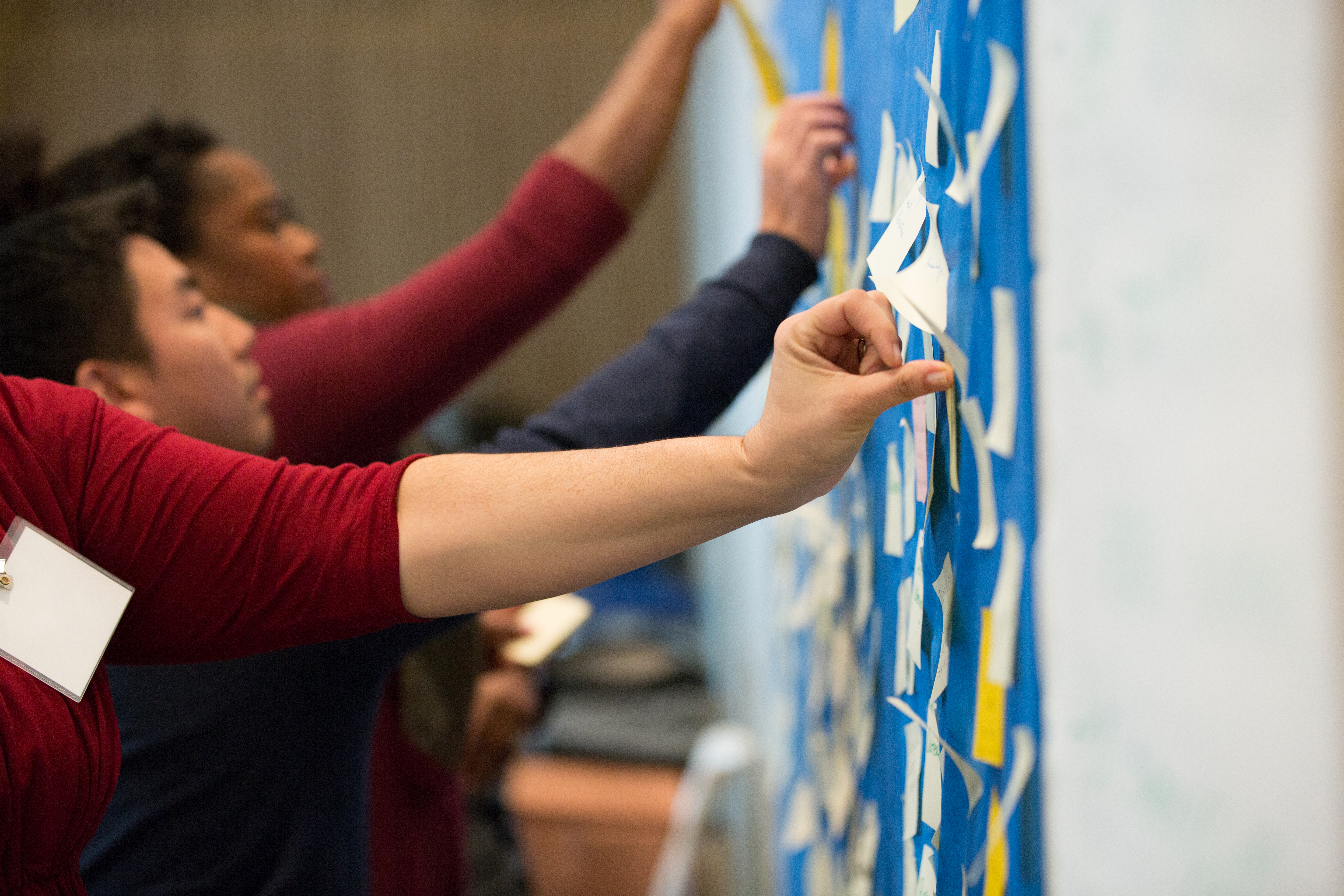 people stick colored Post-it notes onto blue bulletin board
