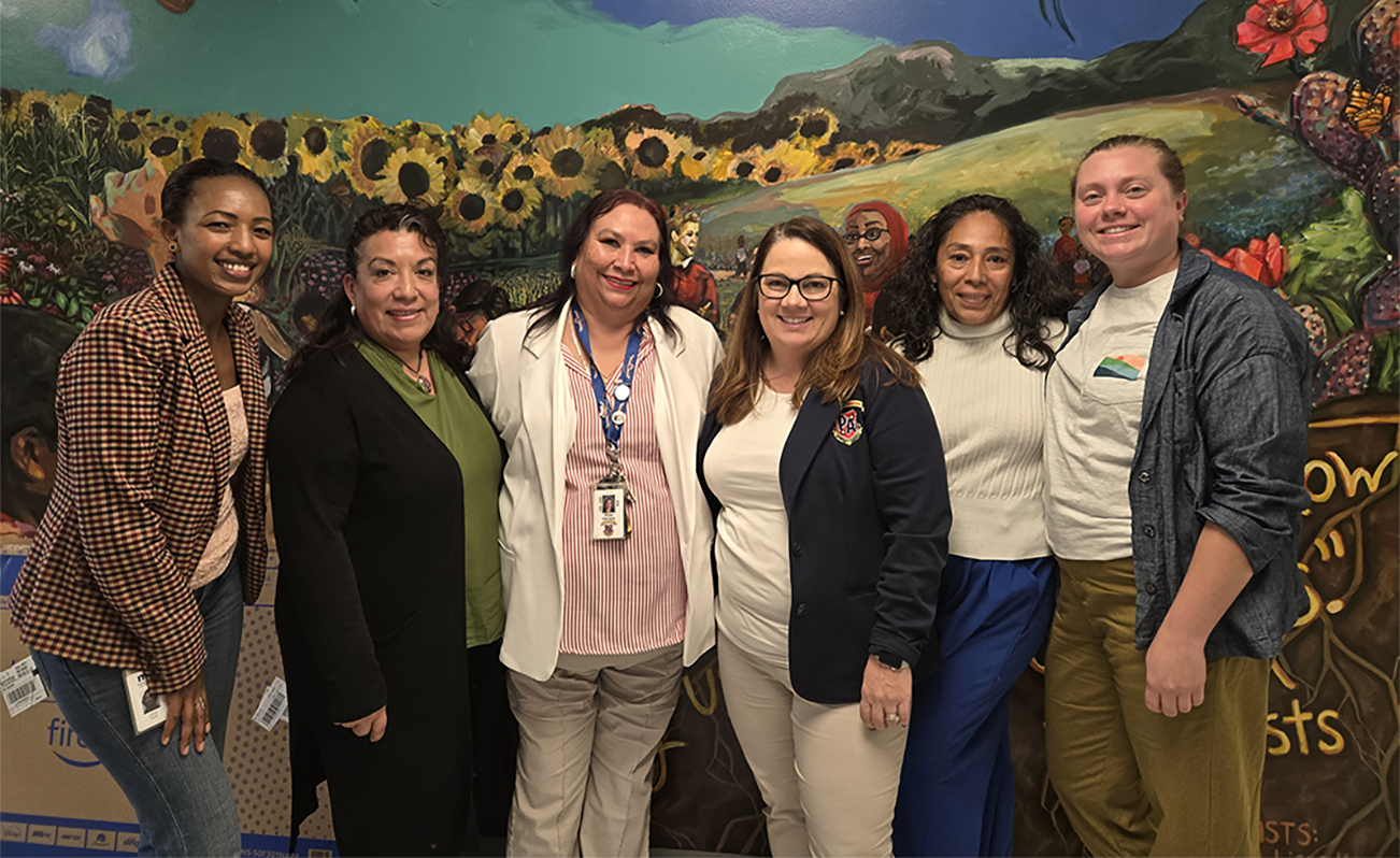grants and capacity team and grantees pose in front of flowered wall mural