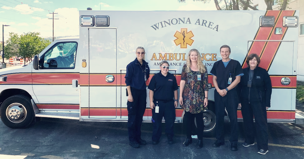 healthcare workers posed in front of an ambulance