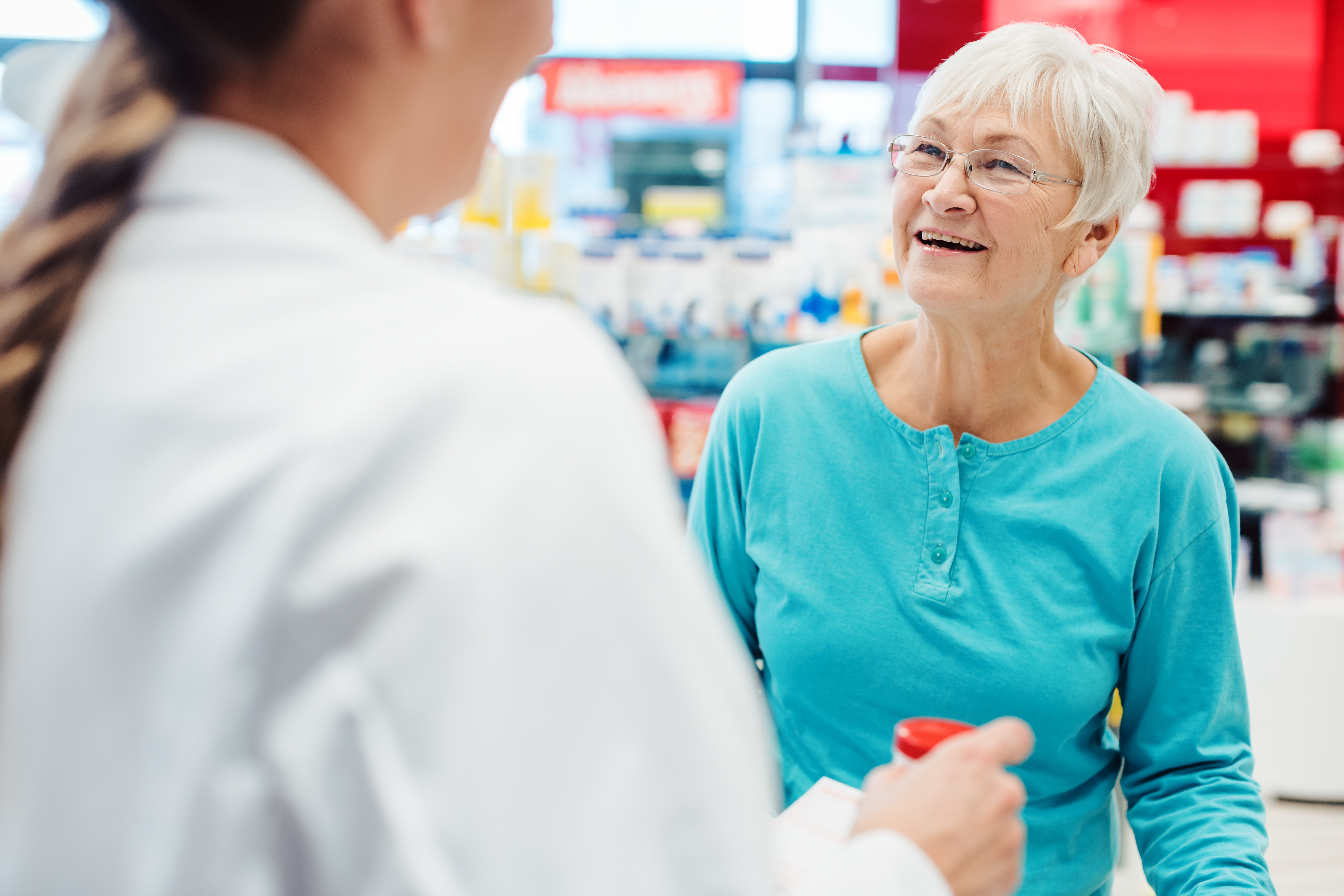an older woman with short hair and glasses talks to a pharmacist
