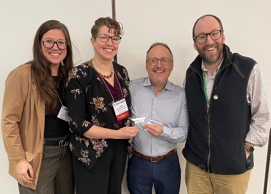 four people stand together smiling and holding award