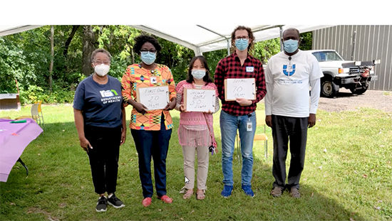 Diverse community clinic staff dressed in street clothes hold shot clinic under tent outdoors